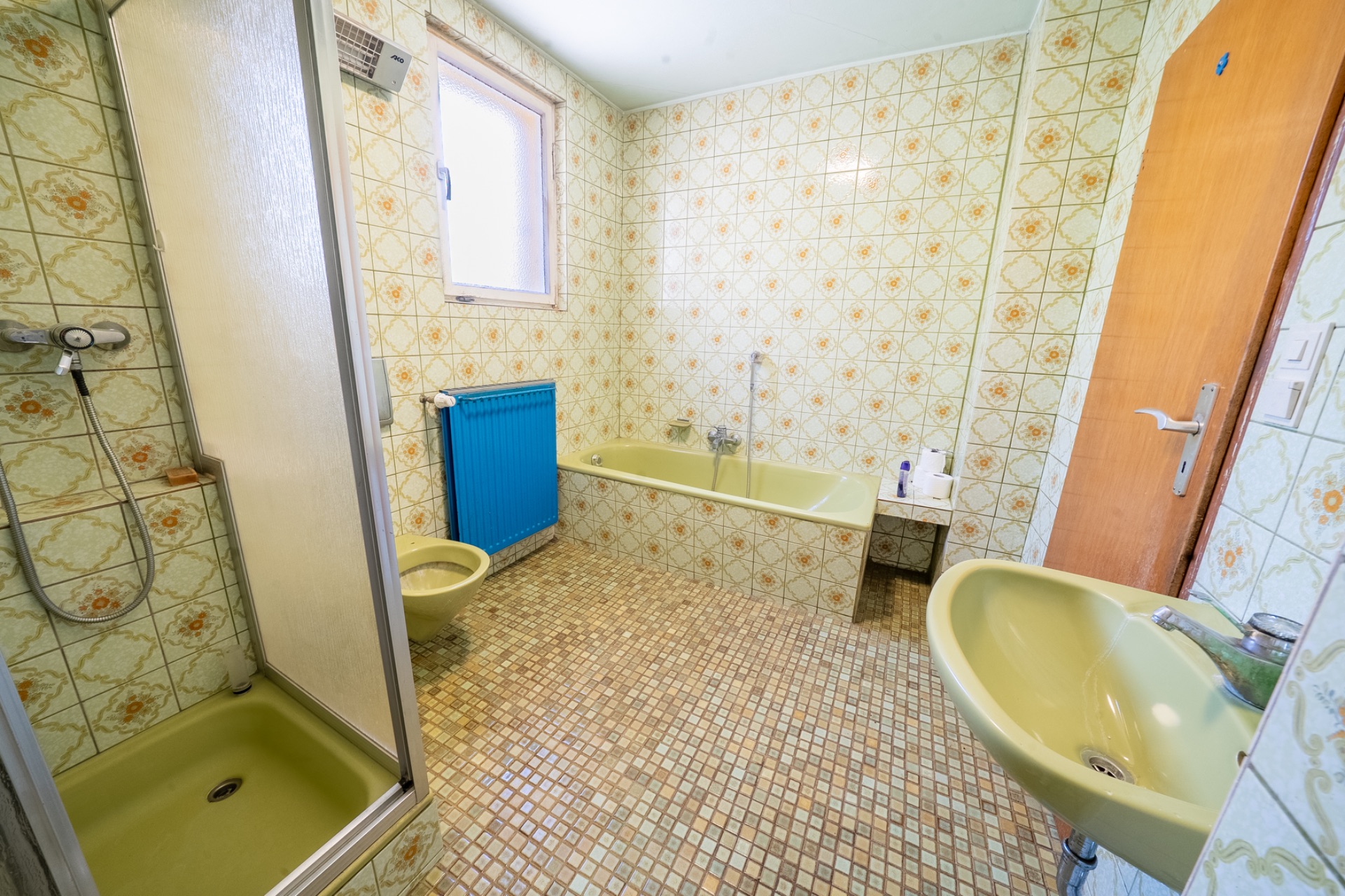 Badezimmer mit gelber Badewanne, Dusche, Waschbecken und Toilette, gemusterte Fliesen an Wand und Boden.