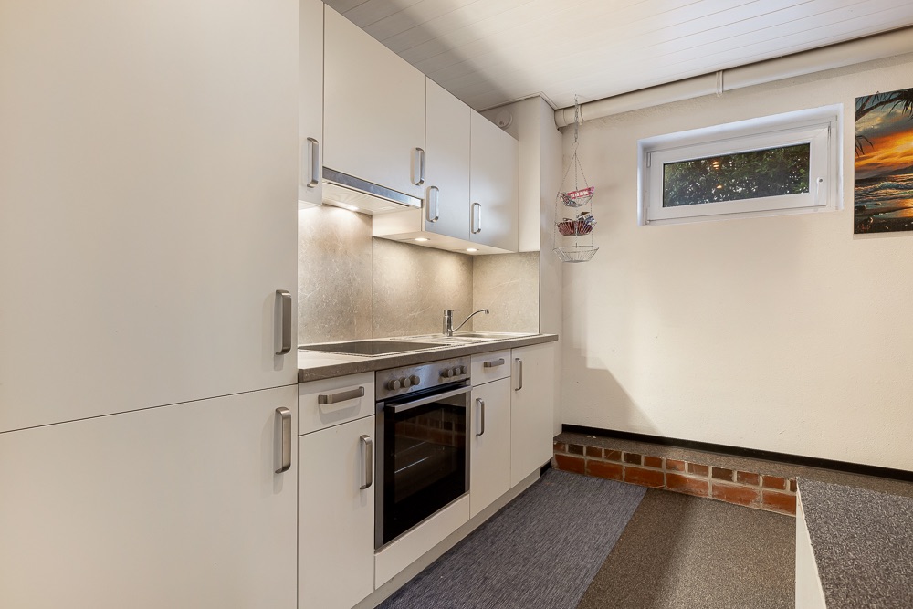 Moderne Einbauküche mit weißen Schränken, Backofen, Spüle und kleinem Fenster an der Wand.