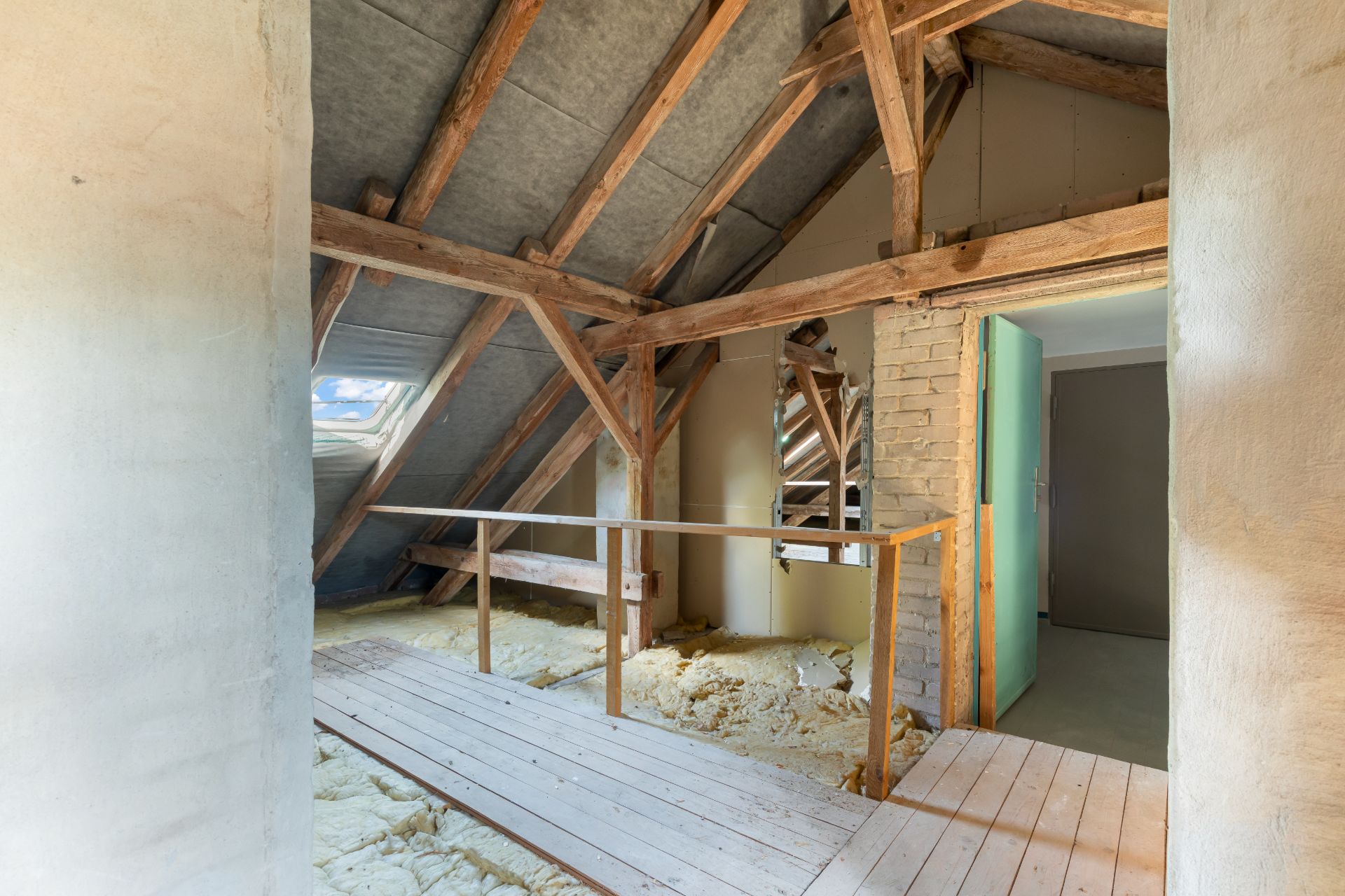 Dachboden mit Holzbalken, Fenster und sichtbarer Dämmung.
