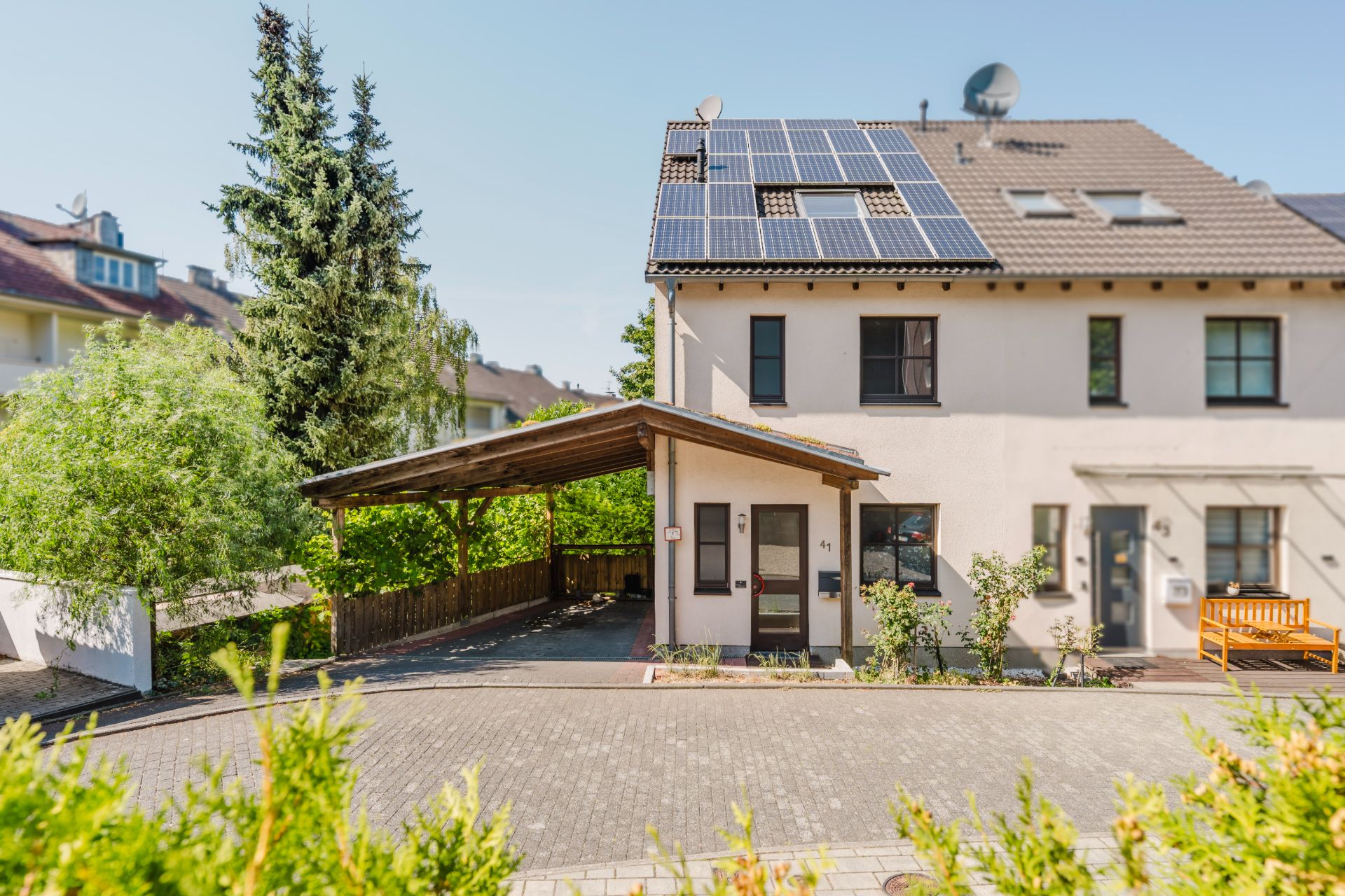 Doppelhaushälfte mit Solarpanels auf dem Dach und Carport an der Seite.
