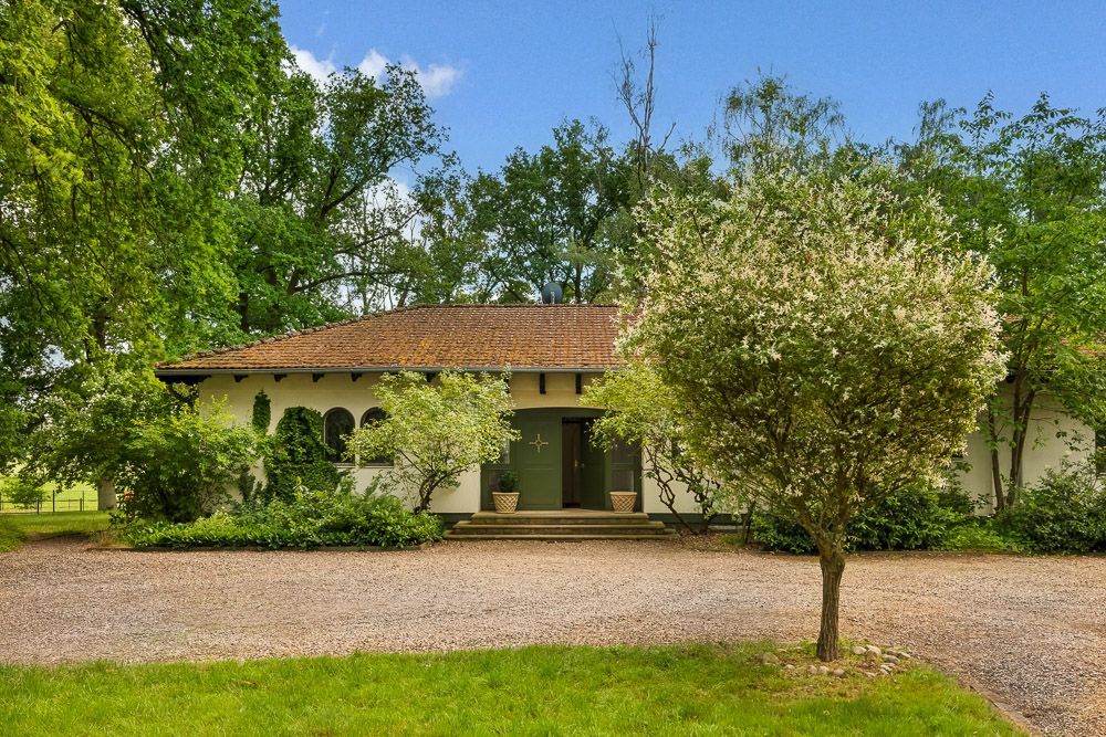 Einfamilienhaus mit Satteldach, umgeben von Bäumen und Büschen, mit Kiesweg vor dem Eingang.