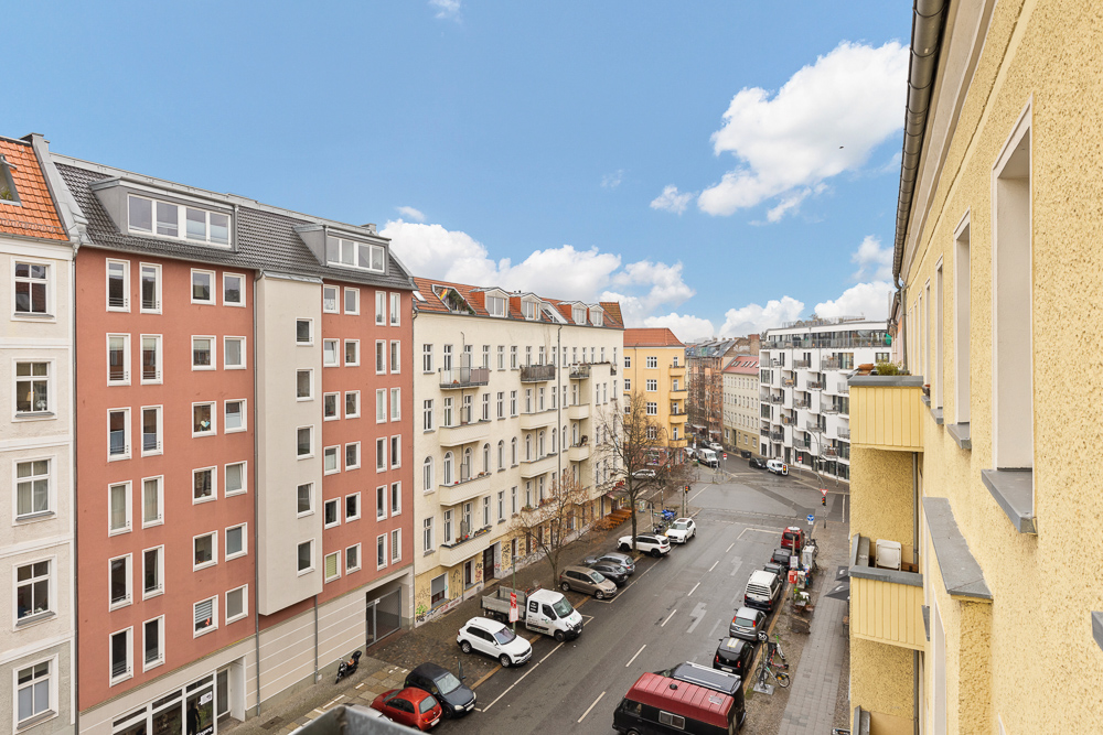 Blick von einem Balkon auf eine ruhige Wohnstraße mit mehreren mehrstöckigen Häusern und geparkten Autos.