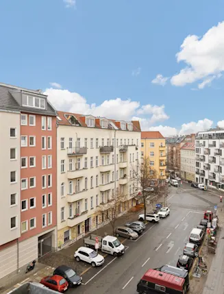 Blick von einem Balkon auf eine ruhige Wohnstraße mit mehreren mehrstöckigen Häusern und geparkten Autos.