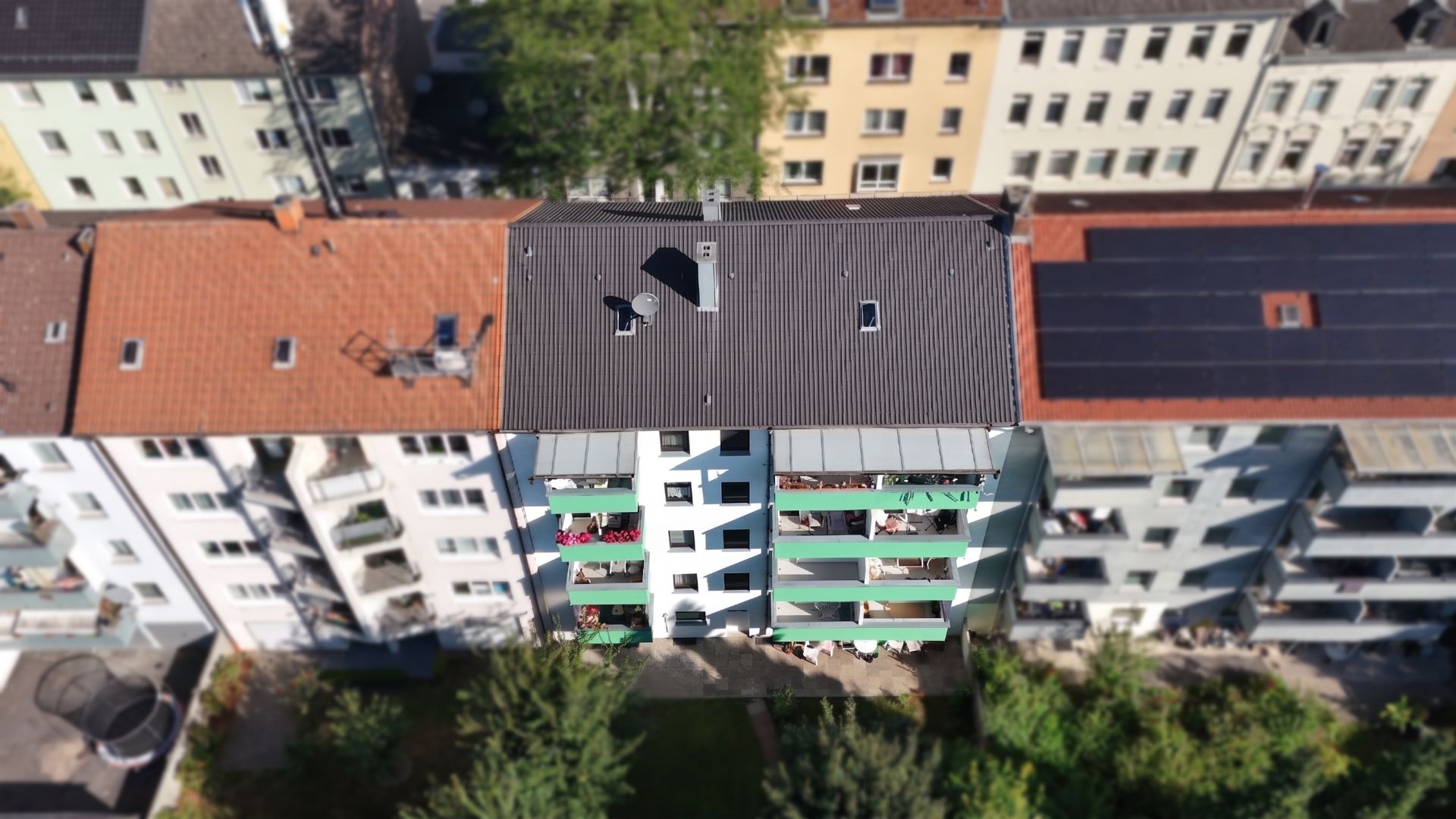 Mehrstöckiges Wohnhaus mit mehreren Balkonen und grünem Garten davor, aus der Vogelperspektive.