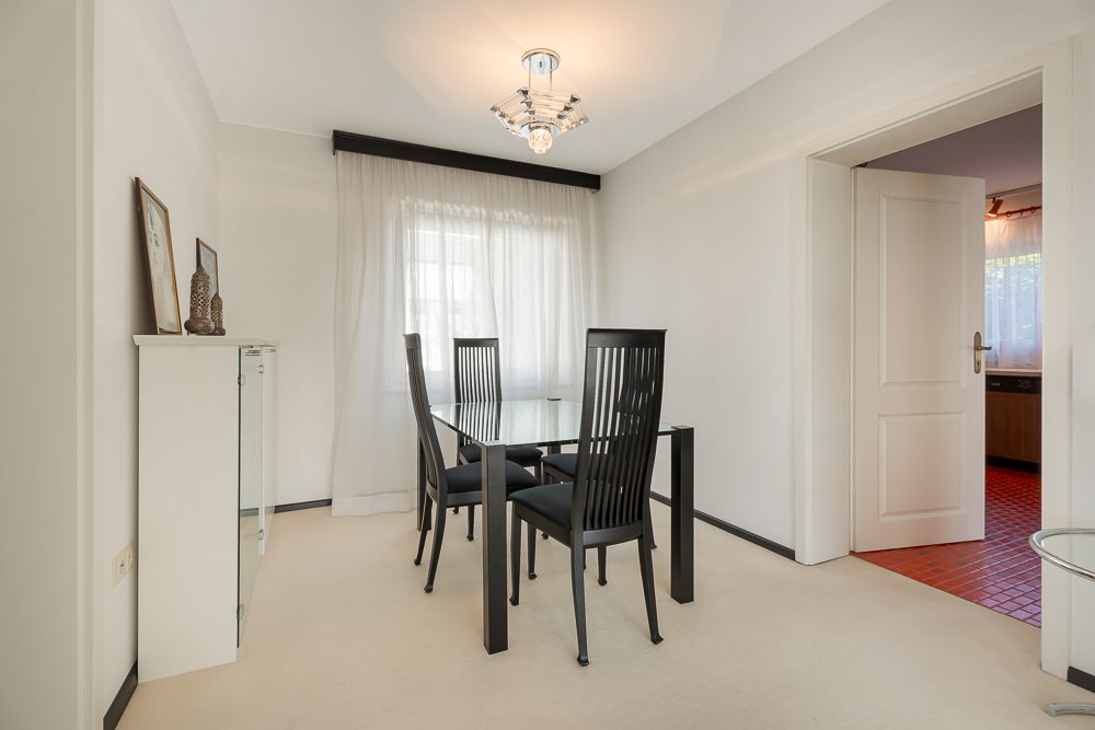 Esszimmer mit Glastisch, vier schwarzen Stühlen und großem Fenster mit Gardinen.