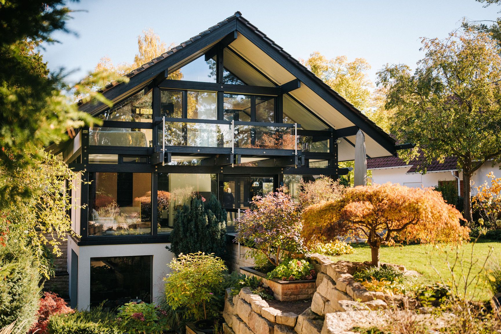 Modernes Wohnhaus mit Glasfassade und Garten, umgeben von Bäumen und Pflanzen.