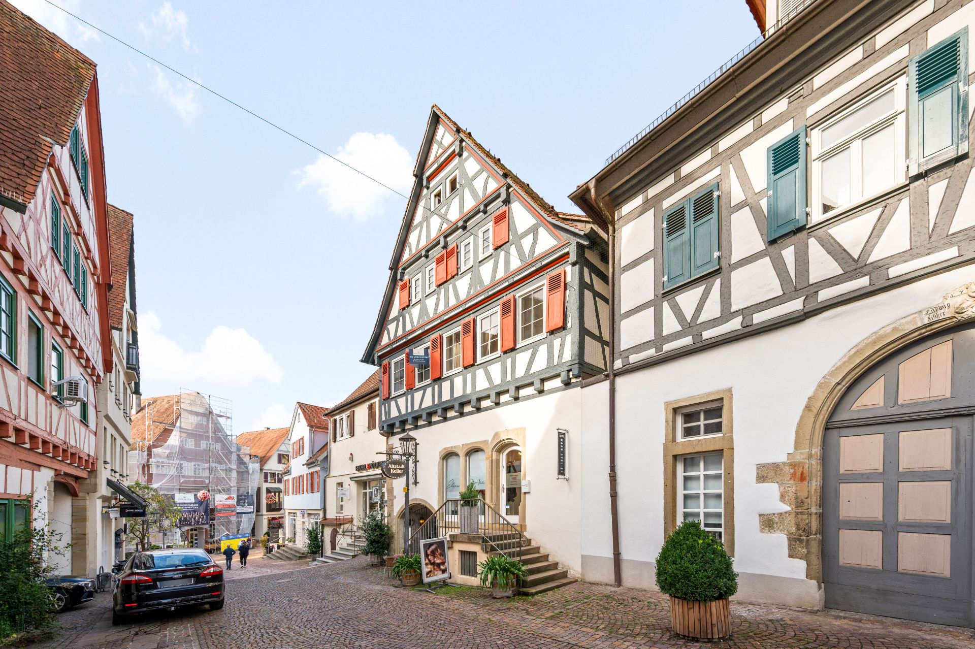 Gepflasterte Straße mit Fachwerkhäusern und Treppen, einige Fußgänger und ein geparktes Auto.