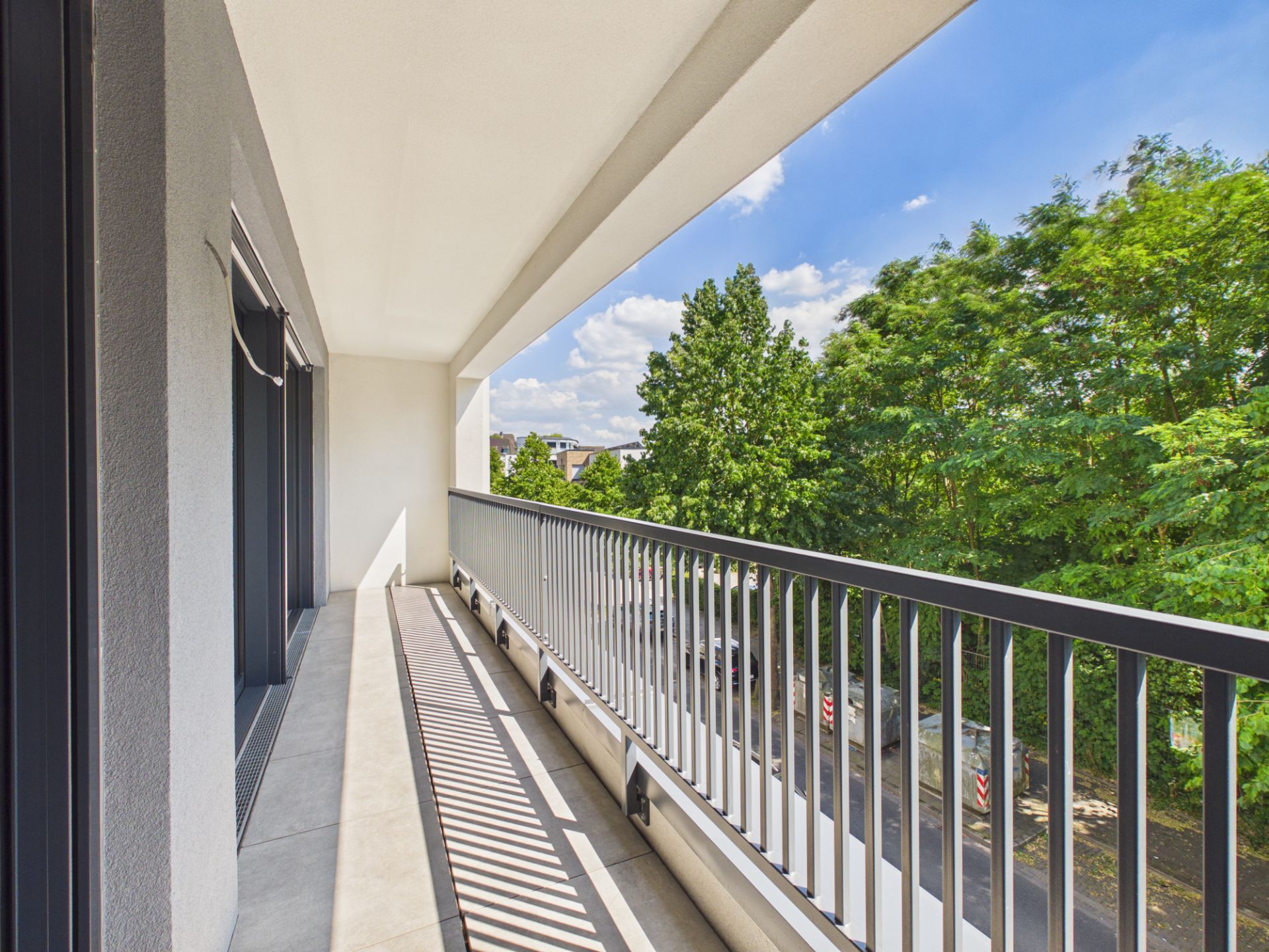 Langer, überdachter Balkon mit Metallgeländer und Blick auf Bäume und eine Straße.