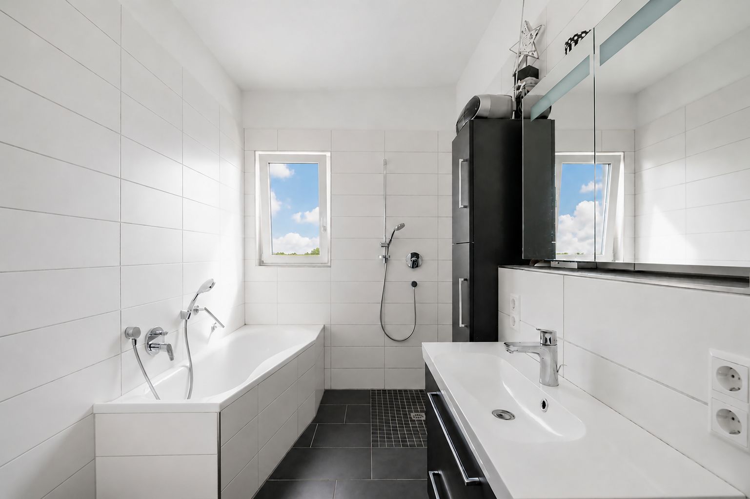 Modernes Badezimmer mit Badewanne, Dusche, Waschbecken und zwei Fenstern.