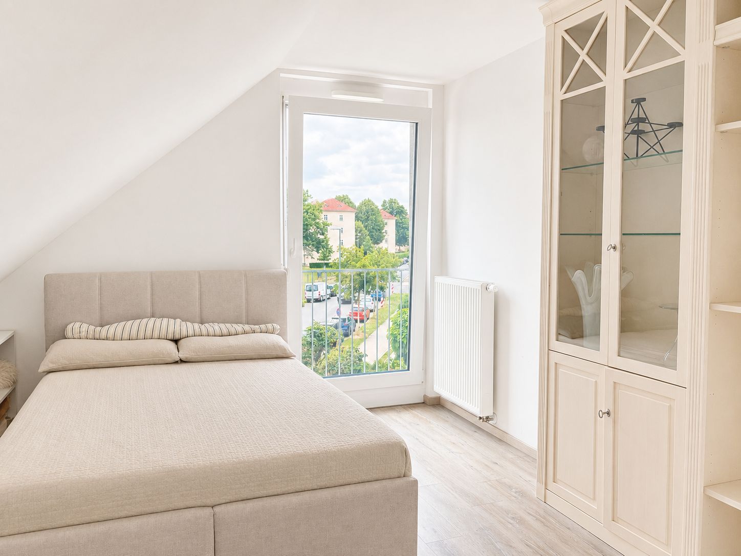 Helles Schlafzimmer mit Bett, großem Fenster und weißem Schrank.