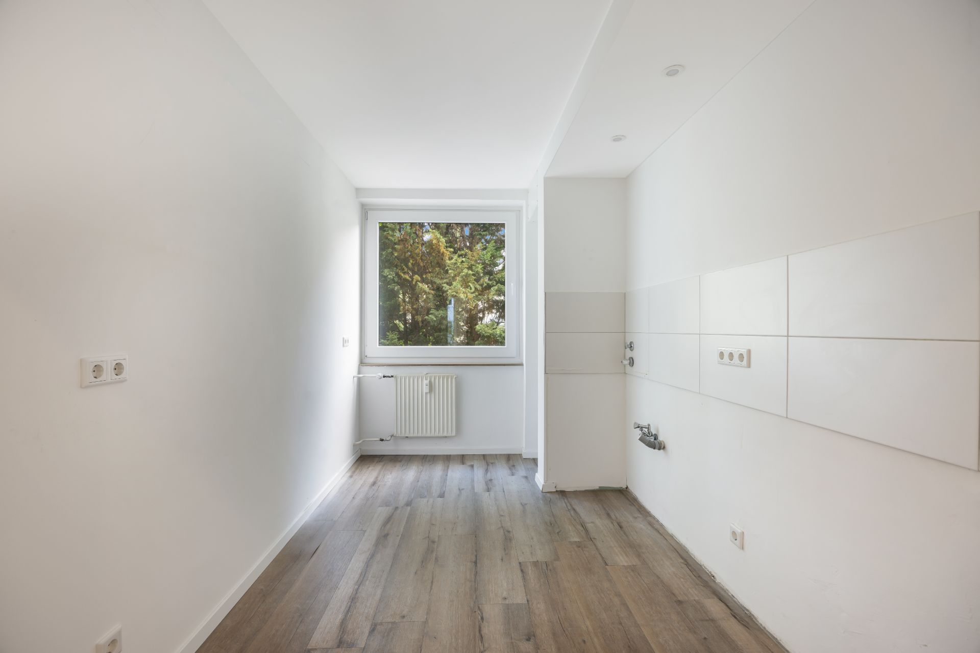 Leerer Raum mit weißer Wand, Fenster, Heizkörper und Holzfußboden.