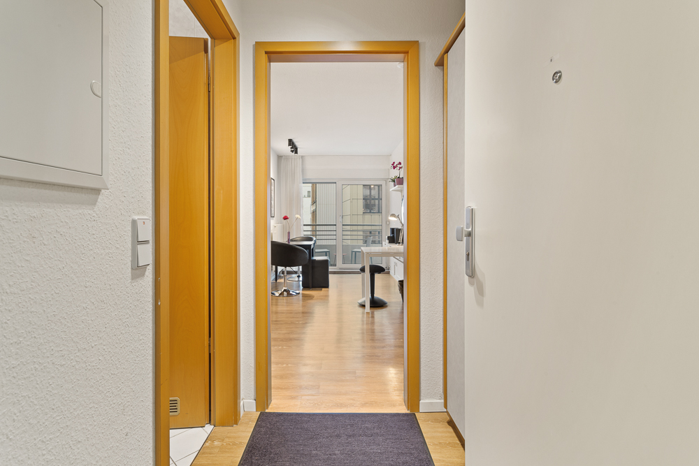 Blick vom Flur in ein helles Wohnzimmer mit Holzboden und moderner Einrichtung.