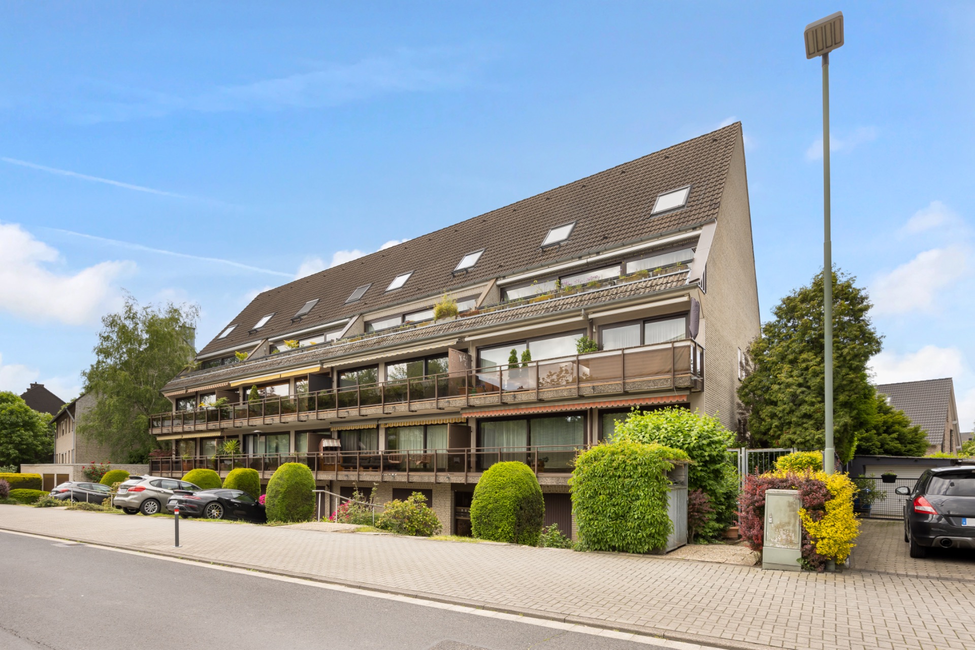 Mehrfamilienhaus mit Balkonen und gepflegtem Vorgarten an einer ruhigen Wohnstraße.