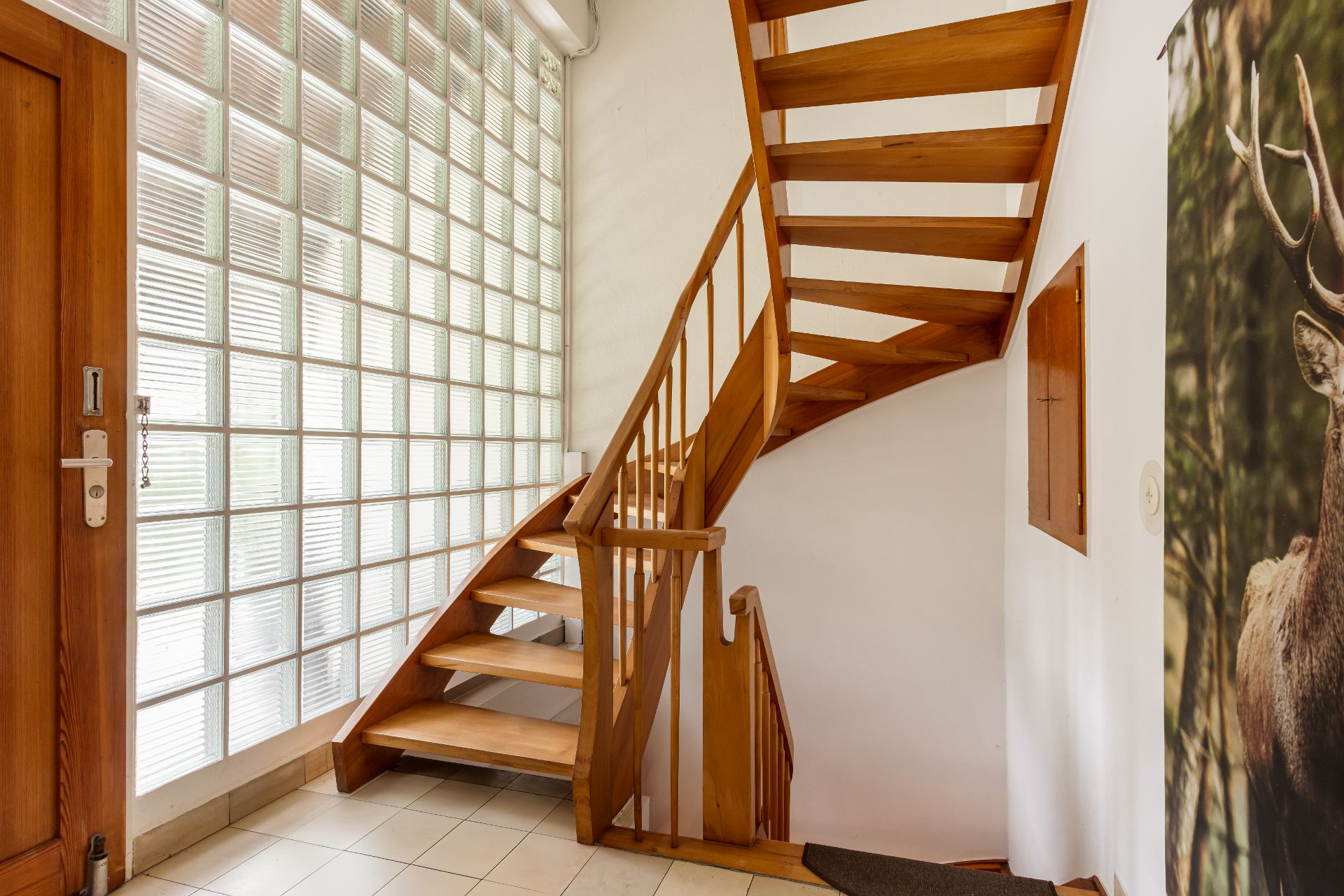 Heller Flur mit Holztreppe, Glasbausteinwand und Kachelboden.