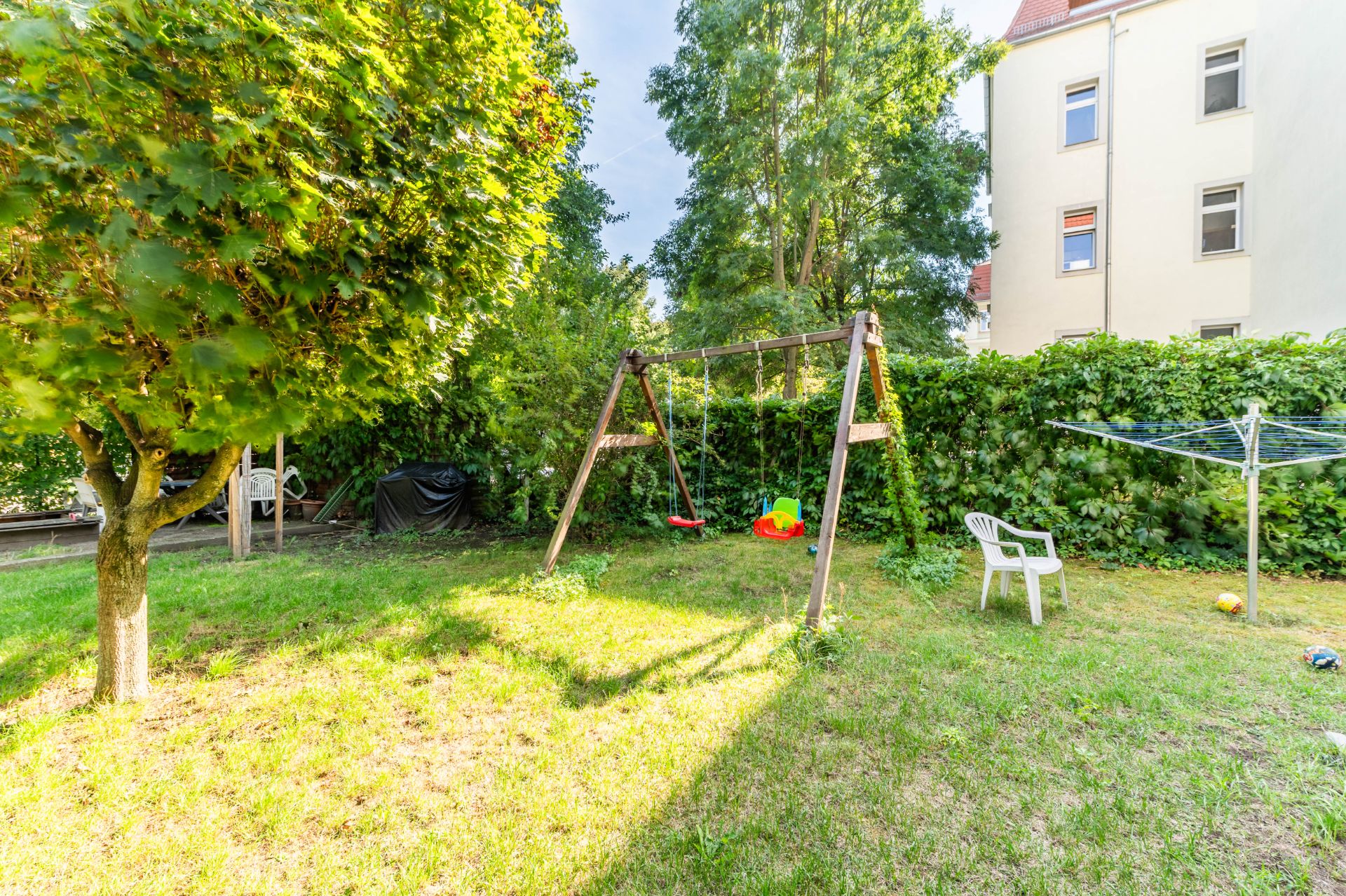 Garten mit Schaukel, Wäscheständer, weißem Stuhl und viel Grün.