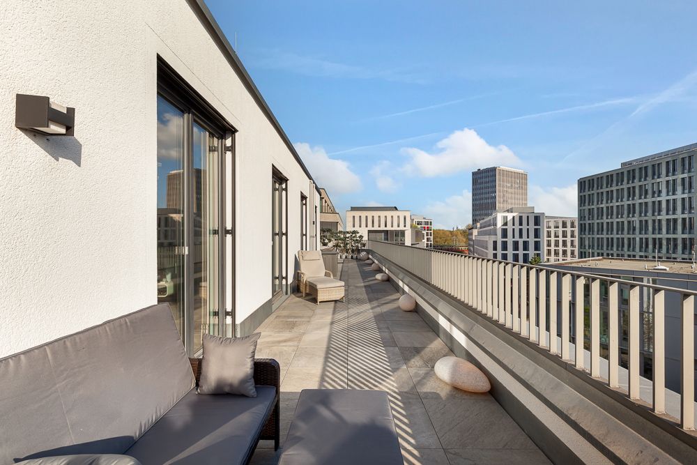 Große Dachterrasse mit Sitzmöbeln und Blick auf moderne Bürogebäude.