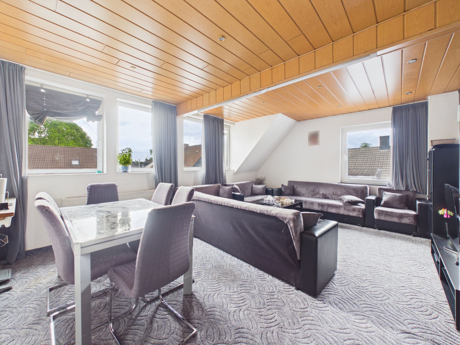 Helles Wohnzimmer mit mehreren Sofas, Esstisch und Stühlen, große Fenster mit Vorhängen.