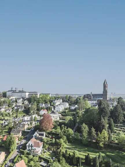 Luftaufnahme von Wohnhäusern, viel Grün und einer Kirche im Hintergrund bei klarem Himmel.