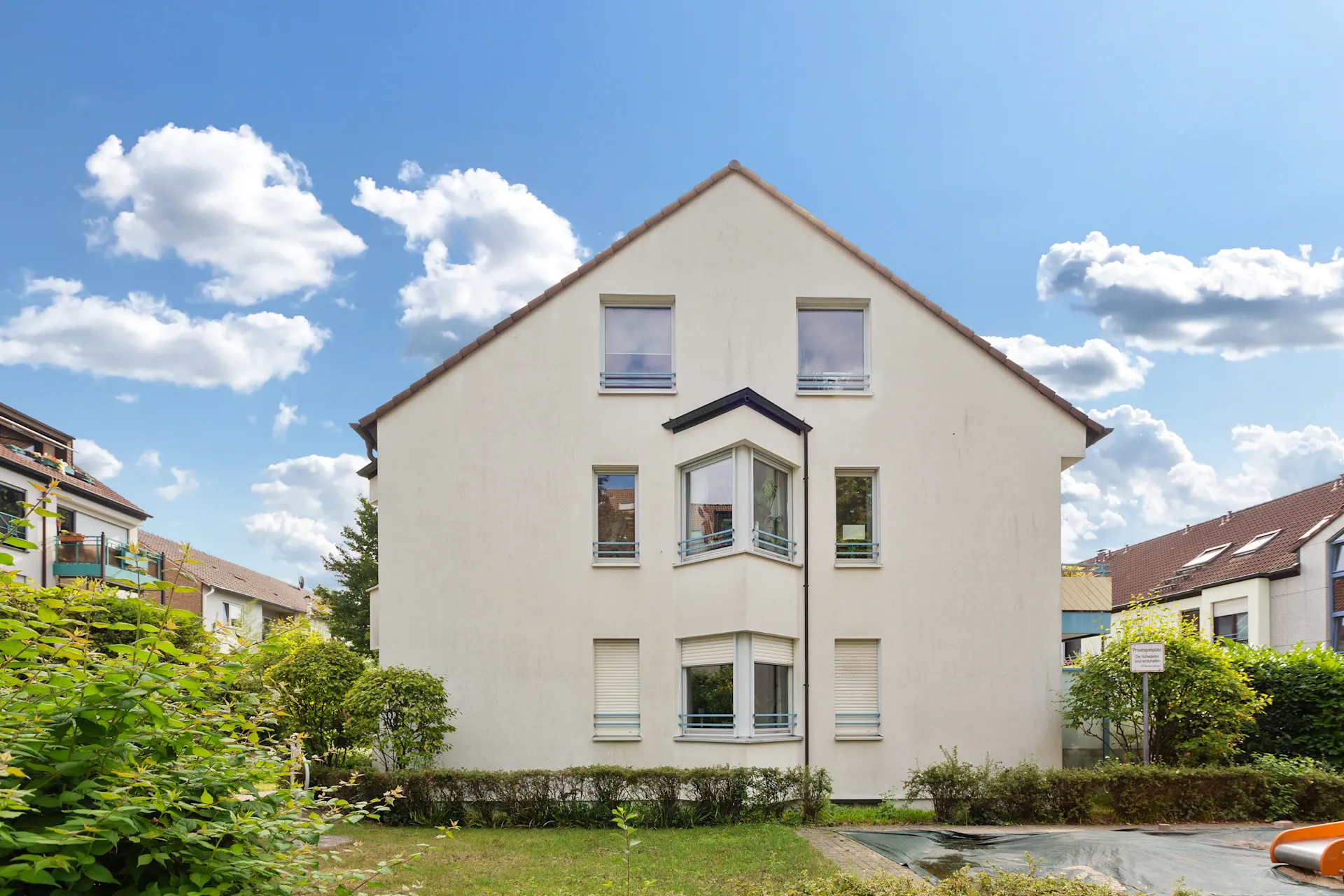 Vorderansicht eines weißen Wohnhauses mit mehreren Fenstern und Garten im Vordergrund.
