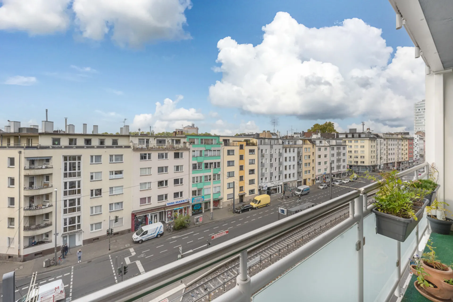 Blick von einem Balkon auf eine Straße mit Wohnhäusern und geparkten Autos.