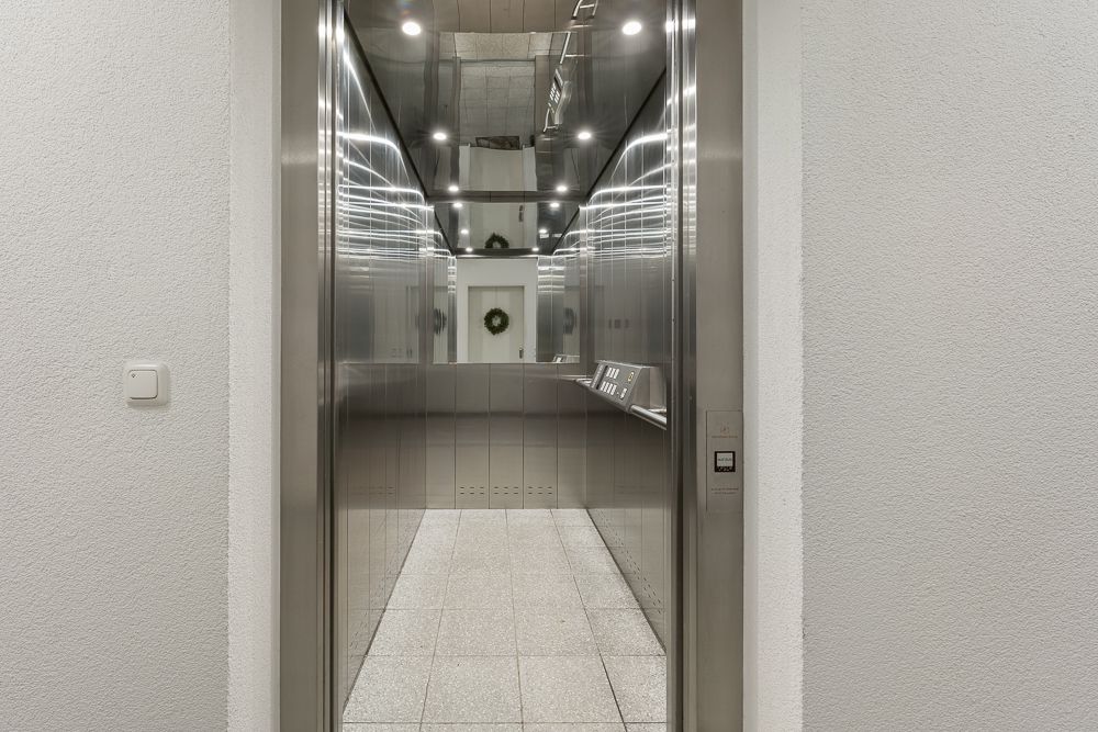Geöffneter Aufzug mit silbernen Wänden und Spiegeldecke in einem Wohngebäude.
