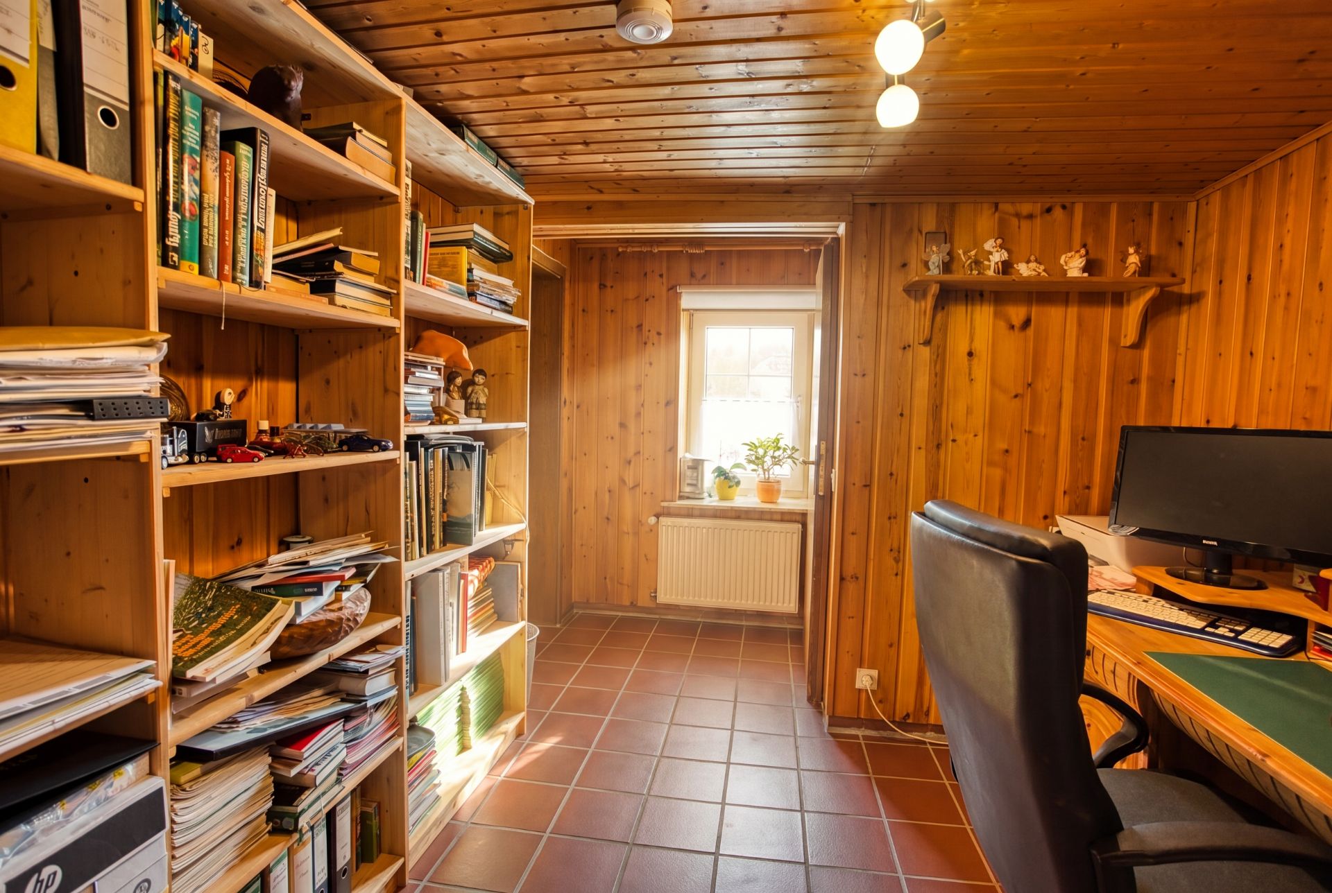 Holzgetäfeltes Arbeitszimmer mit Regalen voller Bücher, Schreibtisch, Stuhl und Fenster mit Blumen.