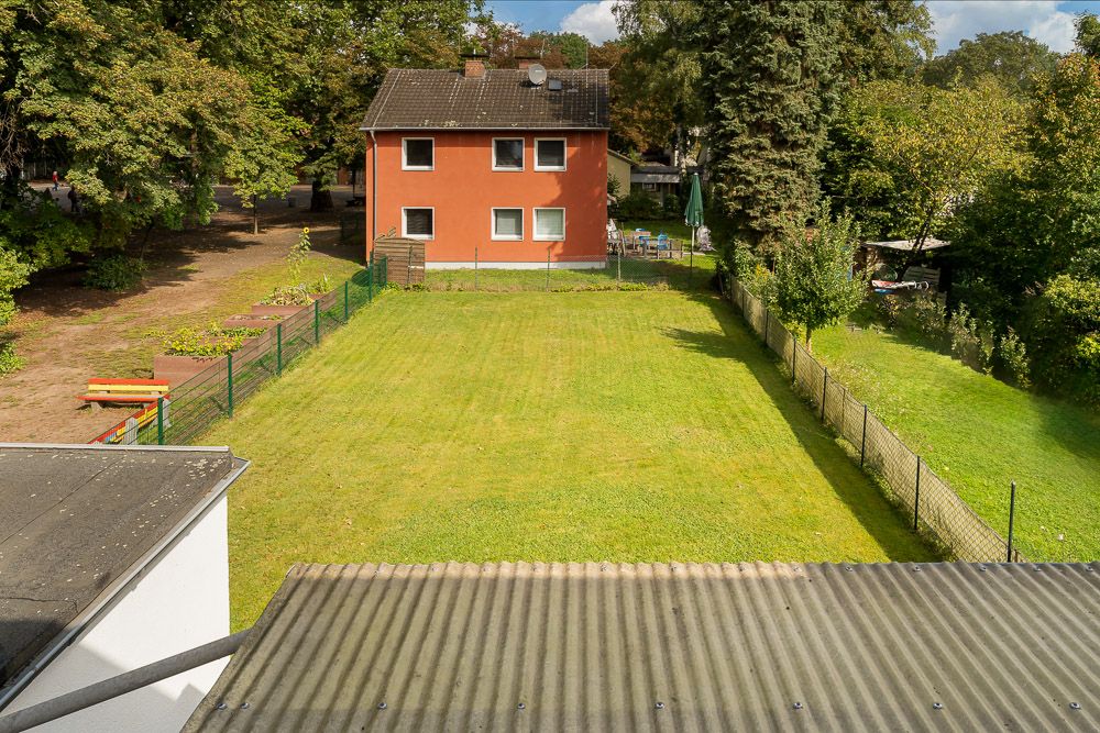 Blick auf einen großen, eingezäunten Garten mit Rasen und einem roten Wohnhaus im Hintergrund.