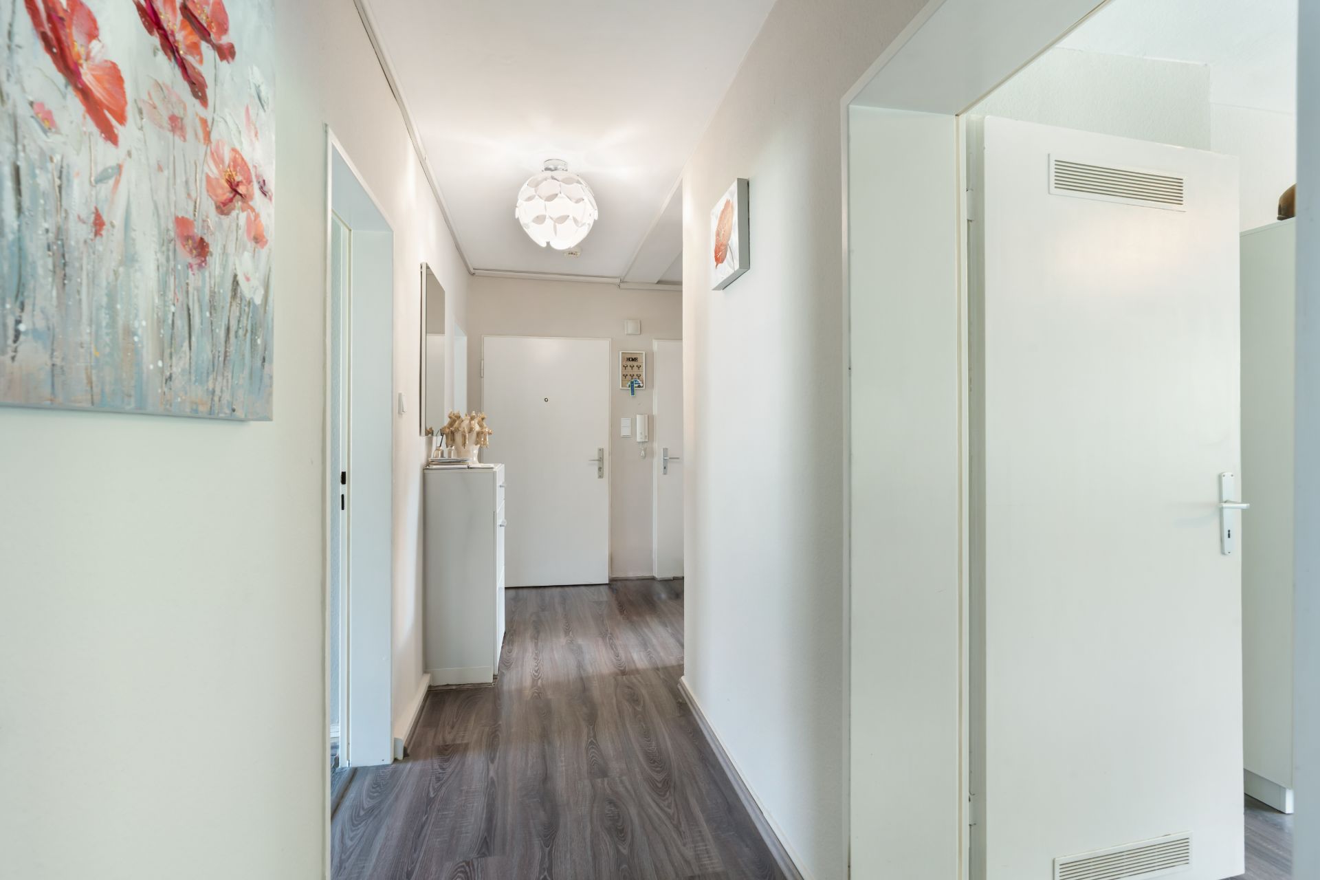 Heller Flur mit Holzboden, weißen Türen und Wandbildern in einer Wohnung.