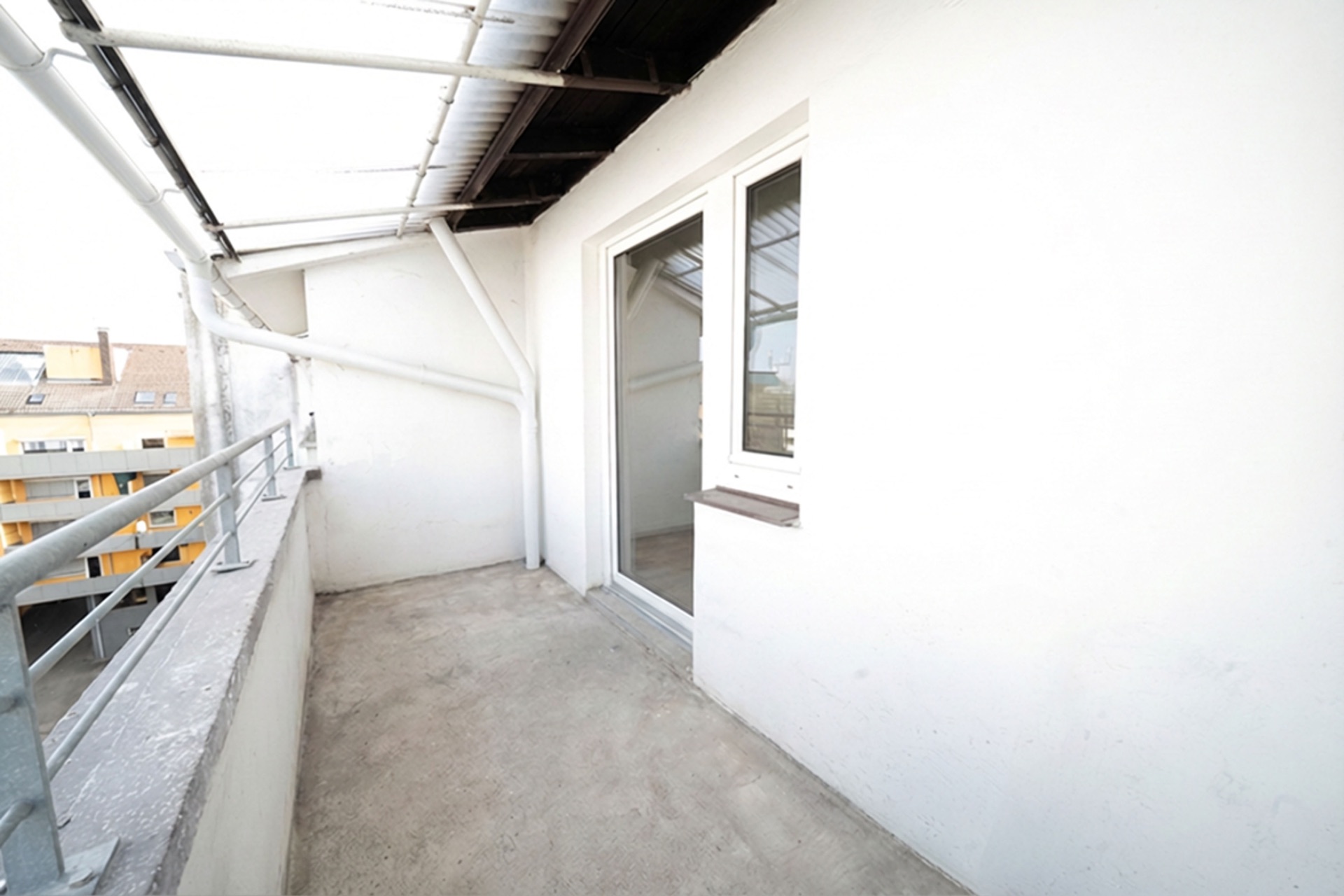 Überdachter Balkon mit Geländer und Zugang durch eine Glastür, helle Hauswand.