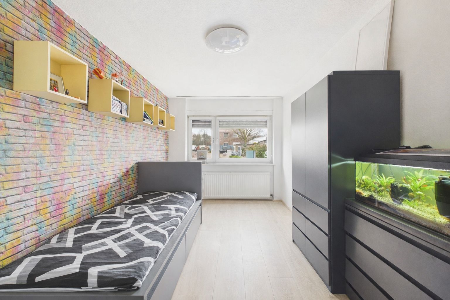 Modernes Schlafzimmer mit bunter Backsteinwand, Einzelbett, Schränken und Aquarium.