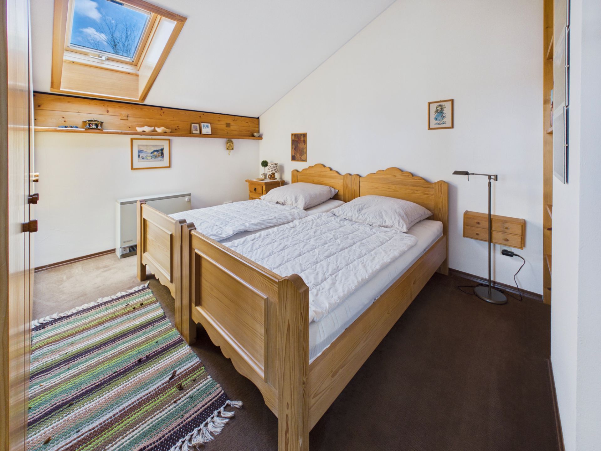 Helles Schlafzimmer mit zwei Holzbett, Teppich und Dachfenster.