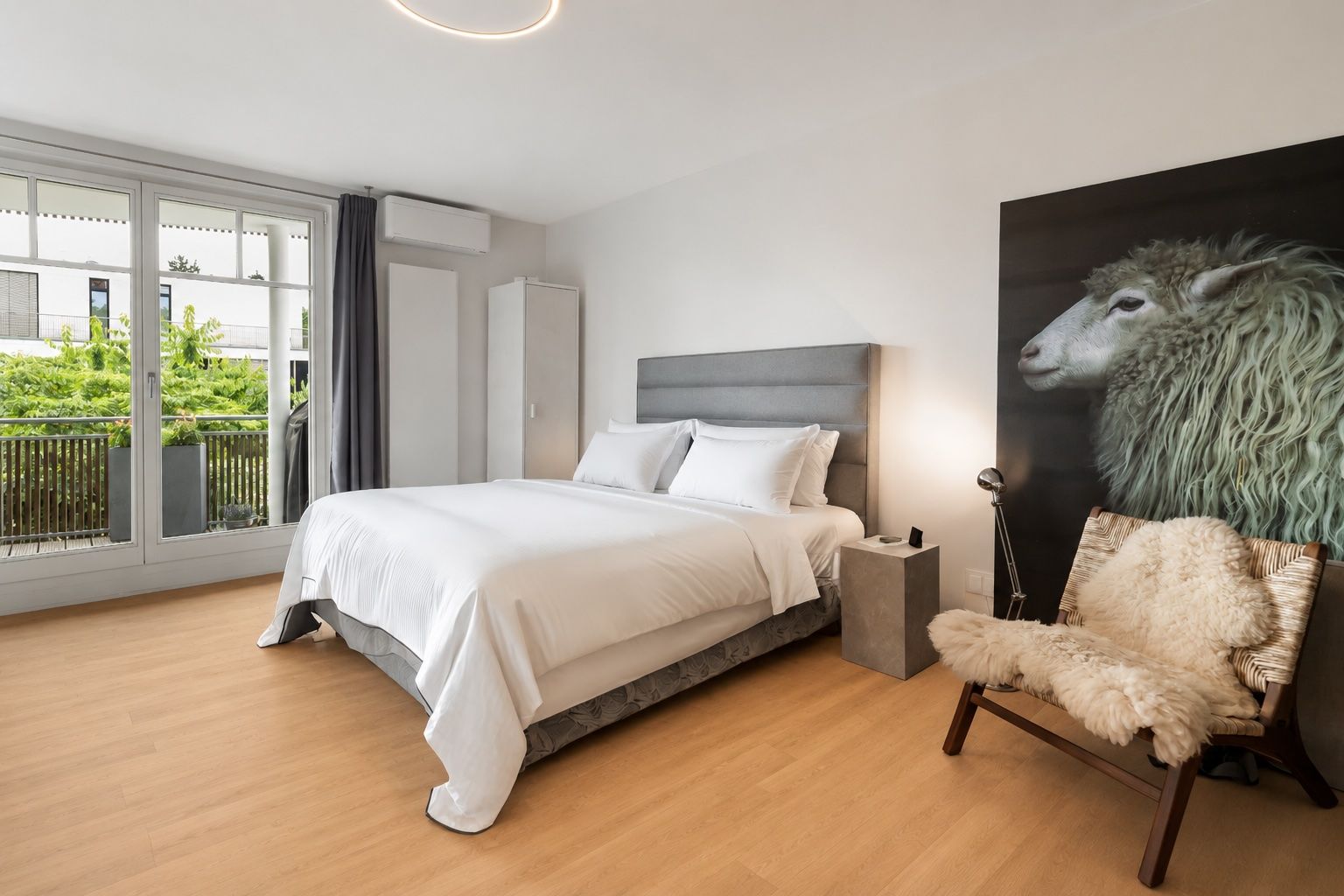 Helles Schlafzimmer mit Doppelbett, großem Fenster, Sessel und Schafbild an der Wand.