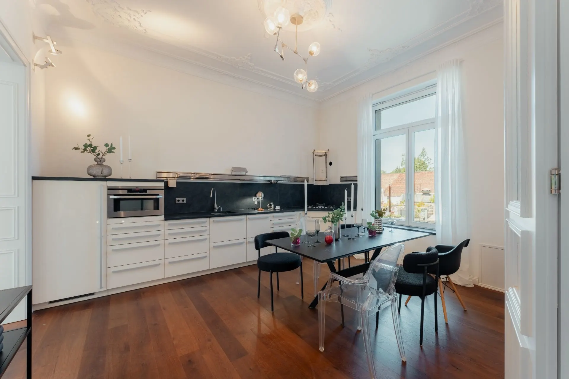 Moderne weiße Küche mit Esstisch und schwarzen Stühlen auf Holzfußboden, großes Fenster im Hintergrund.