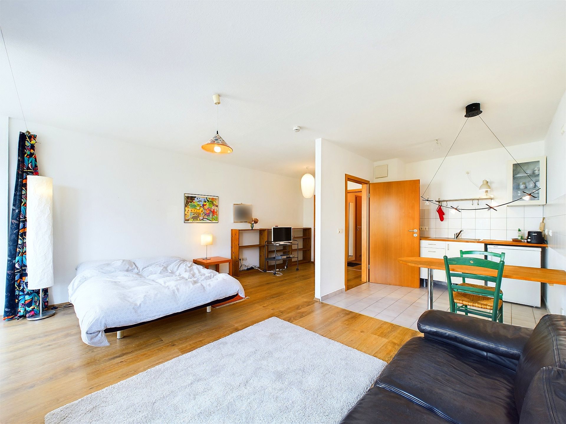 Helles Zimmer mit Bett, Sofa, Teppich, kleinem Küchentisch und Küchenzeile.