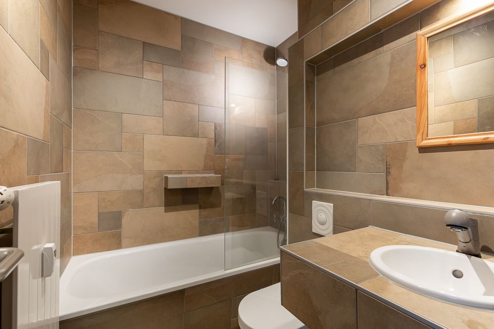 Modernes Badezimmer mit Badewanne, Waschbecken, Spiegel und braunen Wandfliesen.