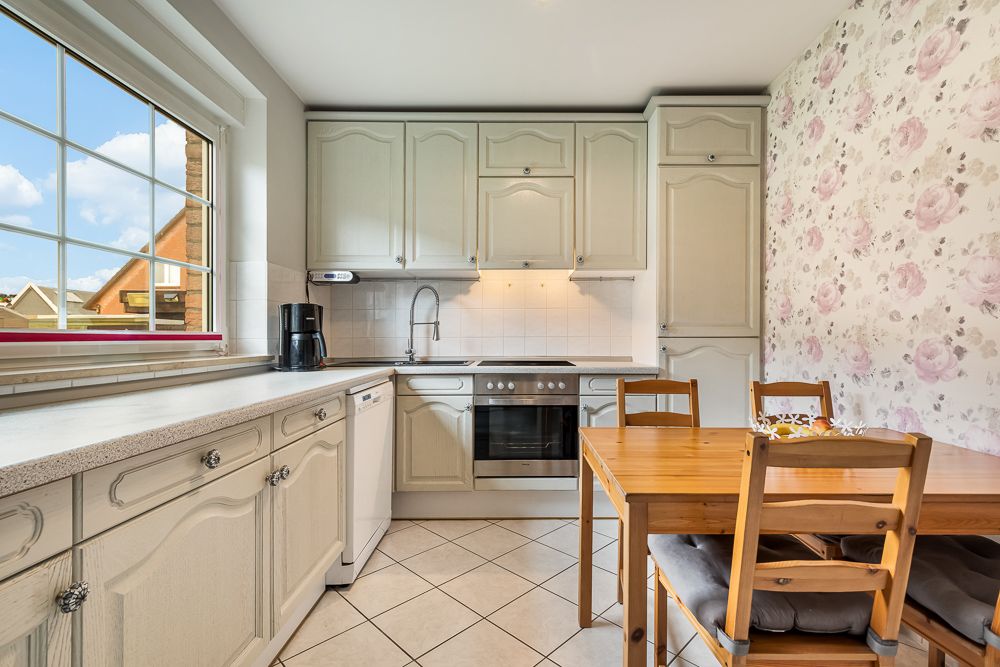 Helle Küche mit Holztisch und Stühlen, weißen Schränken und floral gemusterter Tapete.