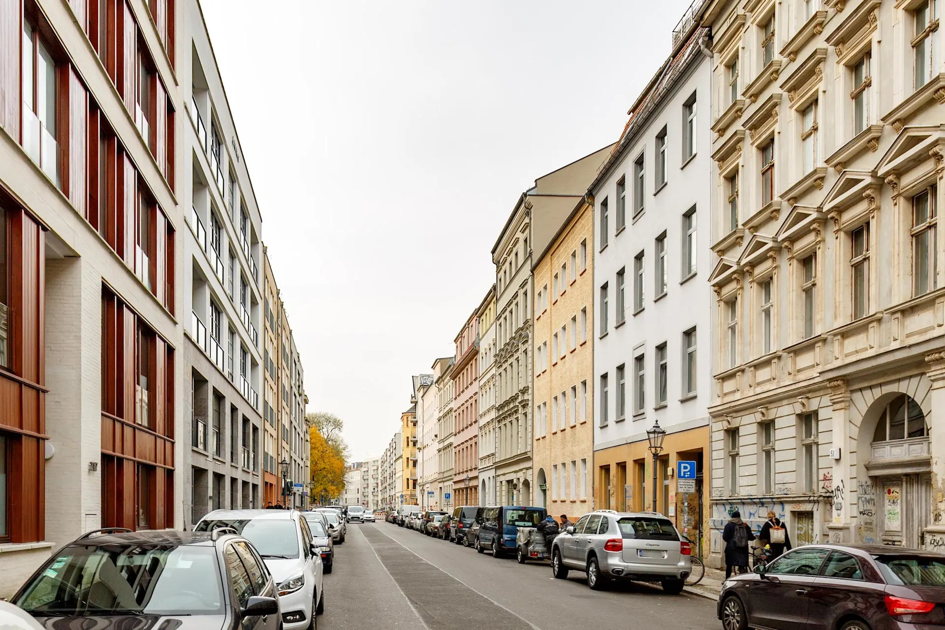 Wohnstraße mit parkenden Autos und mehrstöckigen Wohnhäusern auf beiden Seiten.