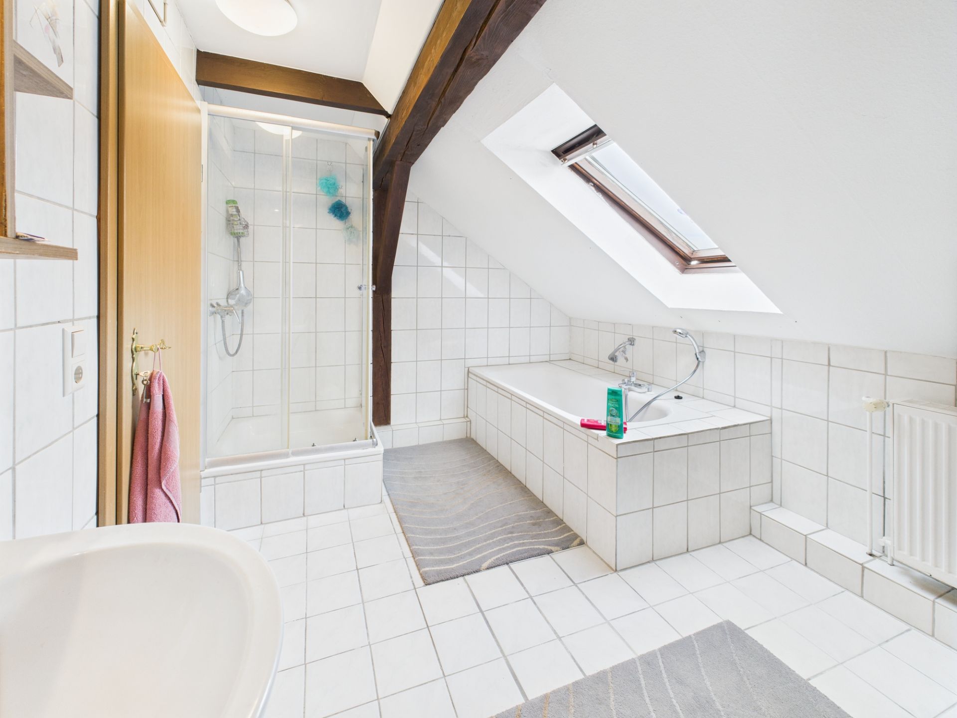 Helles Badezimmer mit Dusche, Badewanne, Dachfenster und weißen Fliesen.
