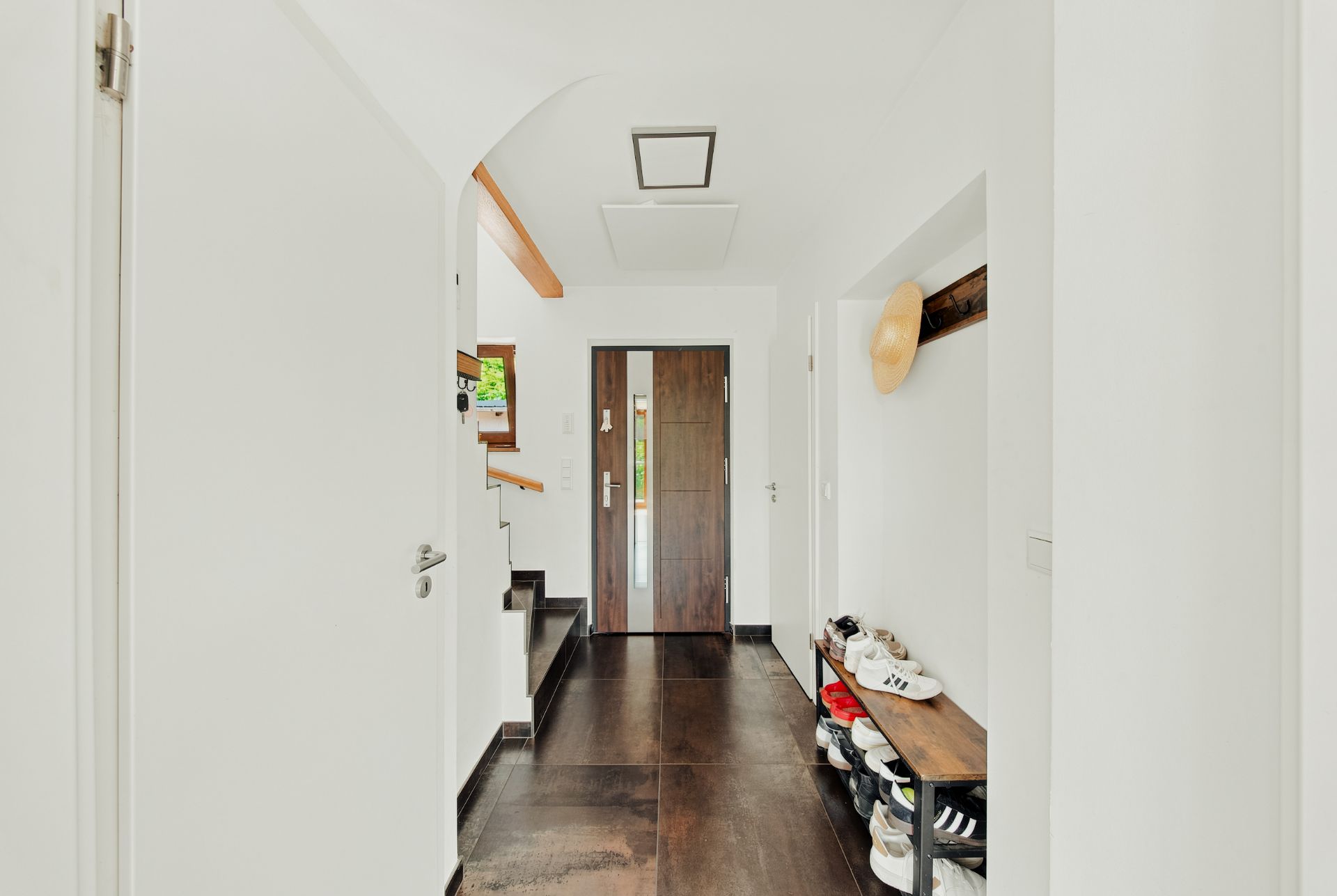 Heller Flur mit Holztür, Schuhregal, Wandhaken und Treppe im Hintergrund.