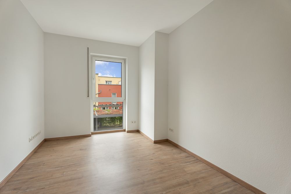 Leerer Raum mit hellen Wänden, Holzfußboden und Fenster mit Blick nach draußen.