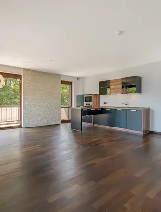 Heller Wohnraum mit Holzboden, offener Küche und großen Fenstern mit Blick ins Grüne.