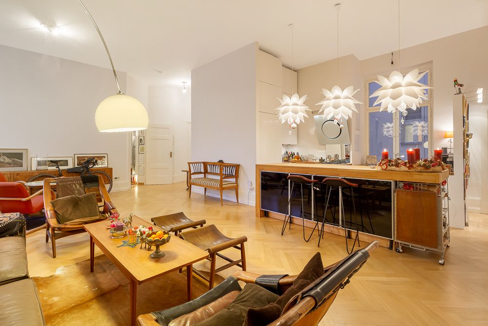 Helles Wohnzimmer mit Holzboden, Sitzgruppe, Esstheke und dekorativen Lampen.