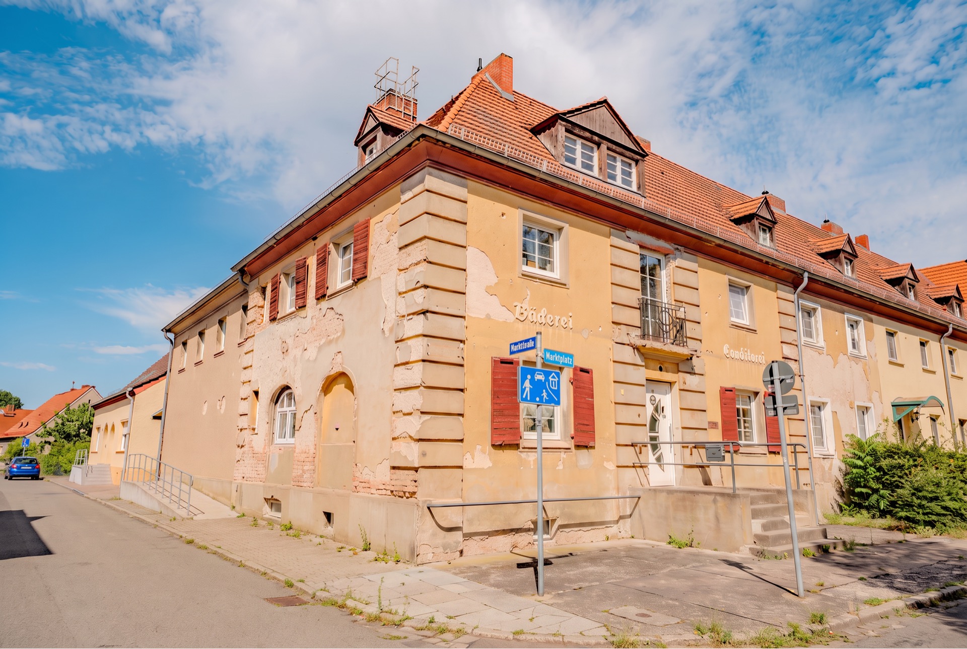 Eckhaus mit gelber Fassade, roten Dachziegeln und abgenutzten Wänden an einer Straßenecke.