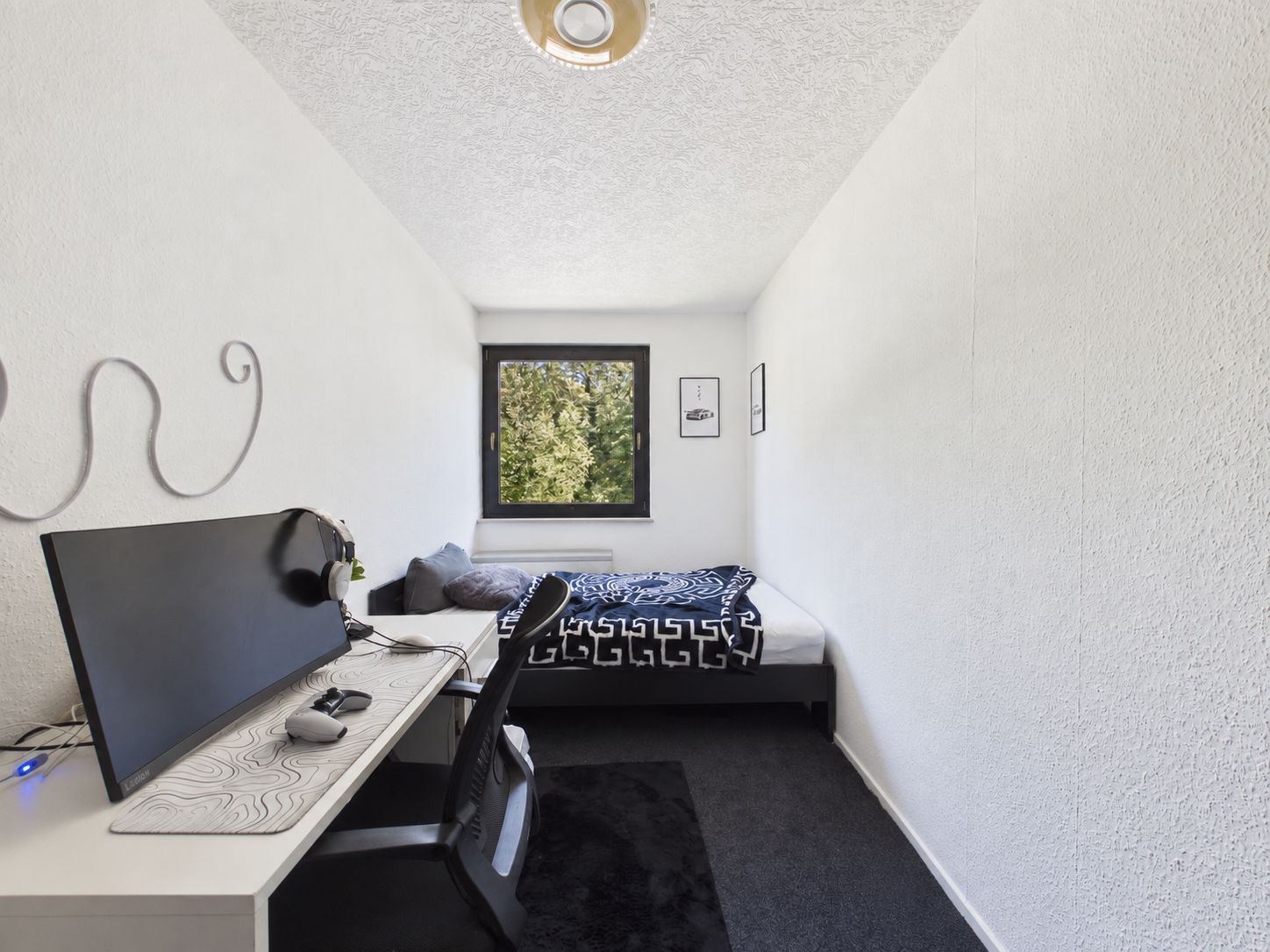 Modernes, schmales Schlafzimmer mit Schreibtisch, Computer, Bett und Fenster mit Blick ins Grüne.
