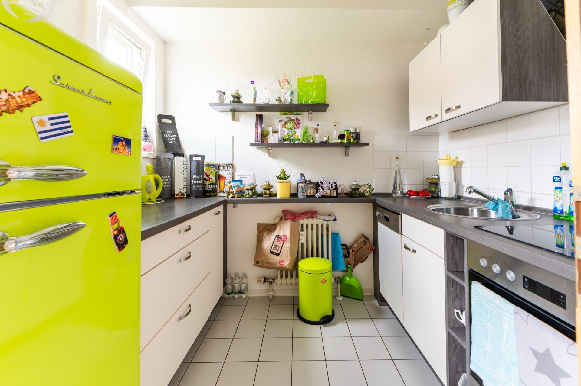 Helle Küche mit grünem Kühlschrank, weißen Schränken und zwei Wandregalen mit Dekorationen.