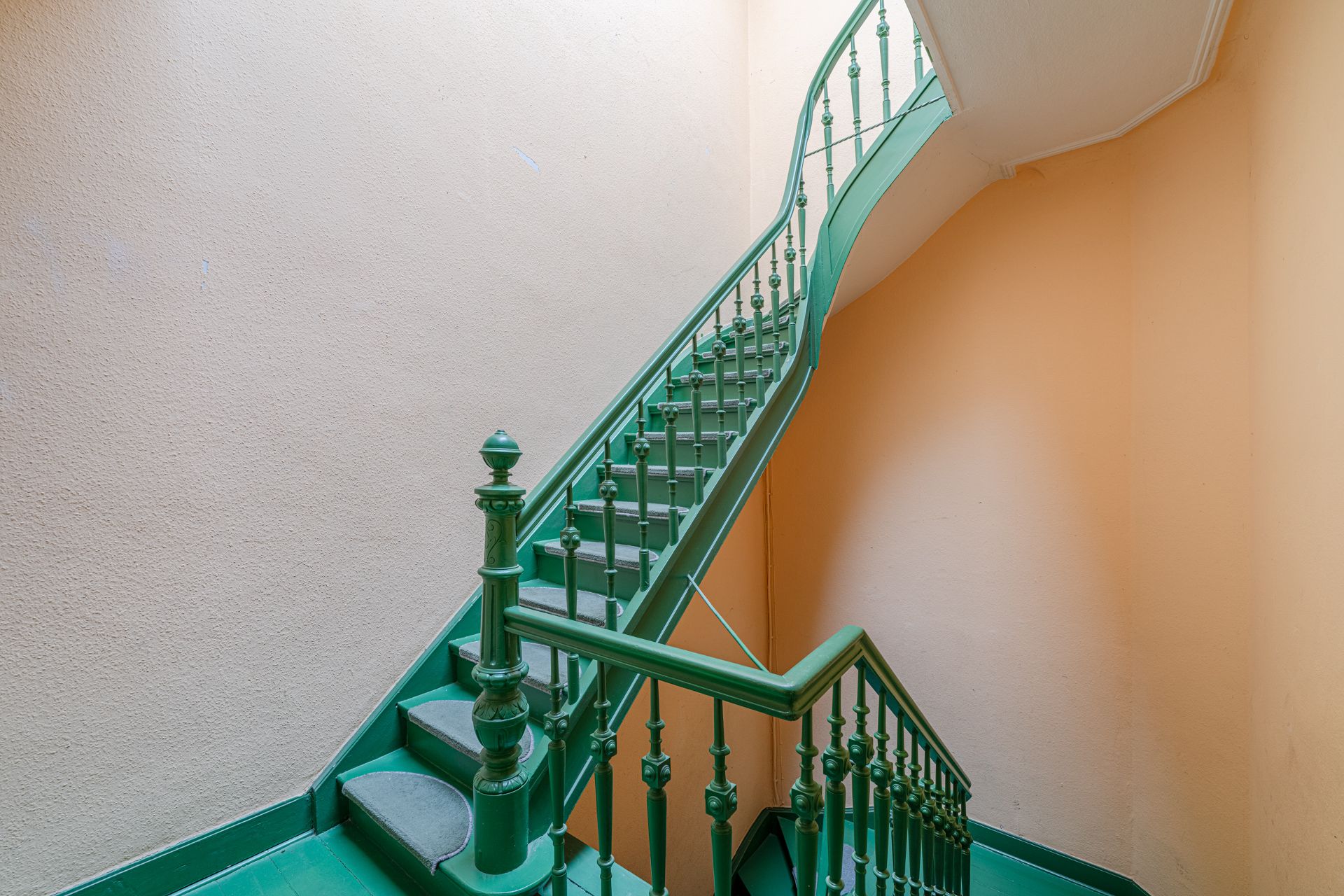 Grünes Treppenhaus mit Geländer in einem Wohngebäude, umgeben von beigen Wänden.
