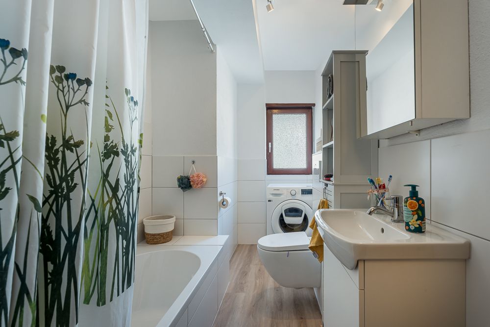 Modernes Badezimmer mit Badewanne, Waschbecken, Toilette, Waschmaschine und Fenster.