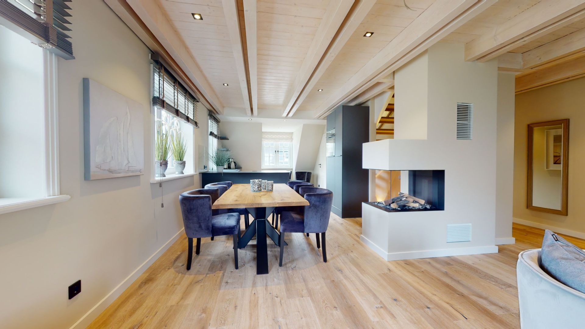 Offenes Esszimmer mit Holztisch, sechs Stühlen, Kamin und Treppe im Hintergrund.