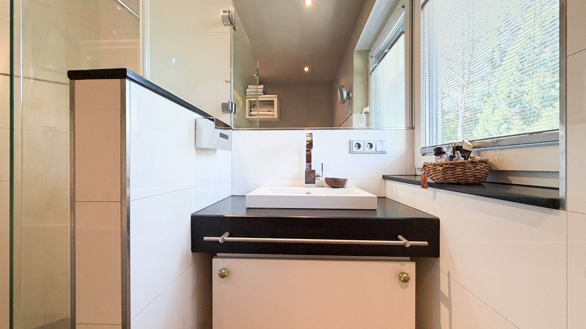 Modernes Badezimmer mit Waschbecken, Spiegel, großem Fenster und Ablage mit Korb.