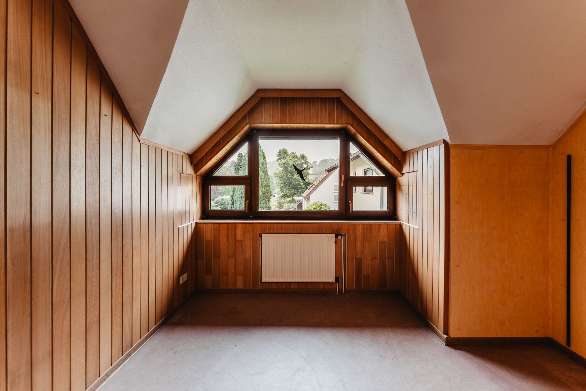Leerer Raum mit Holzvertäfelung, großem Fenster und Heizkörper unter dem Fenster.